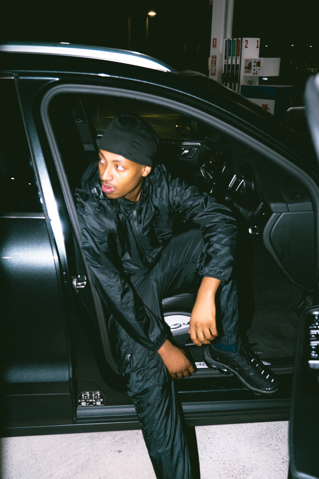 SWISHER J seated in an open car doorway during a night shoot